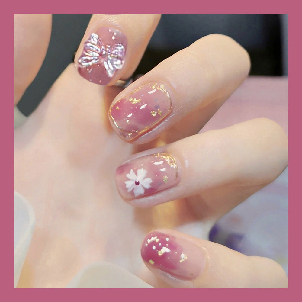 Close-up of a hand with pink nail polish featuring floral designs.