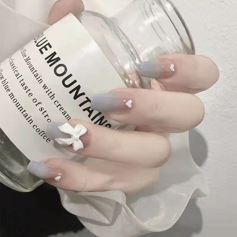 A set of press-on nails featuring a coffin shape with a 3D bow accent, in shades of purple and blue, held against a white background with a label reading 'Blue Mountain Coffee'.