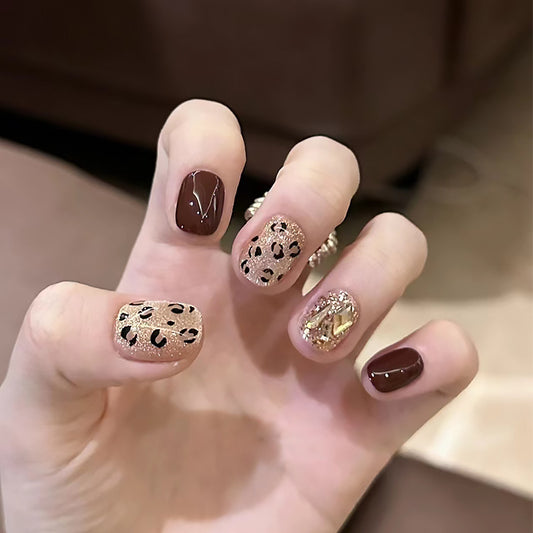 A set of press-on nails featuring a glossy, burgundy and gold cheeta print design.