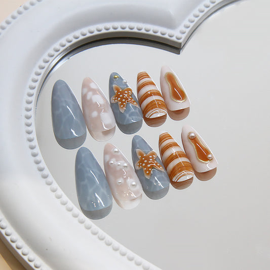 A set of false nails with a gray and cream marbled design, featuring a starfish motif, displayed on a white heart-shaped mirror.