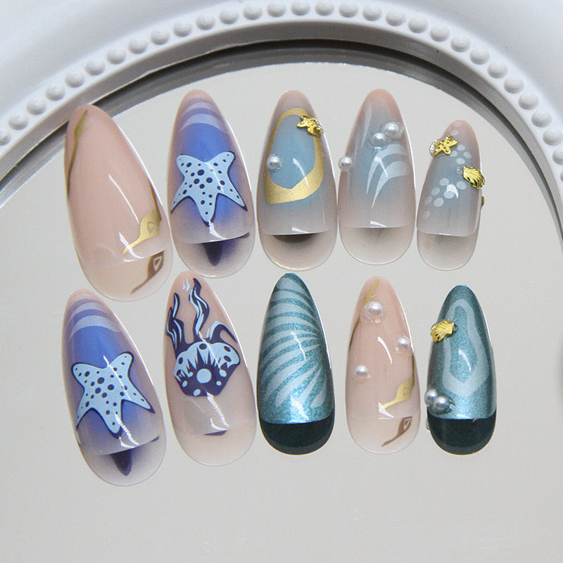 A set of almond-shaped nails in pastel blue and pink colors, featuring seashell and pearl accents, displayed on a white plate.