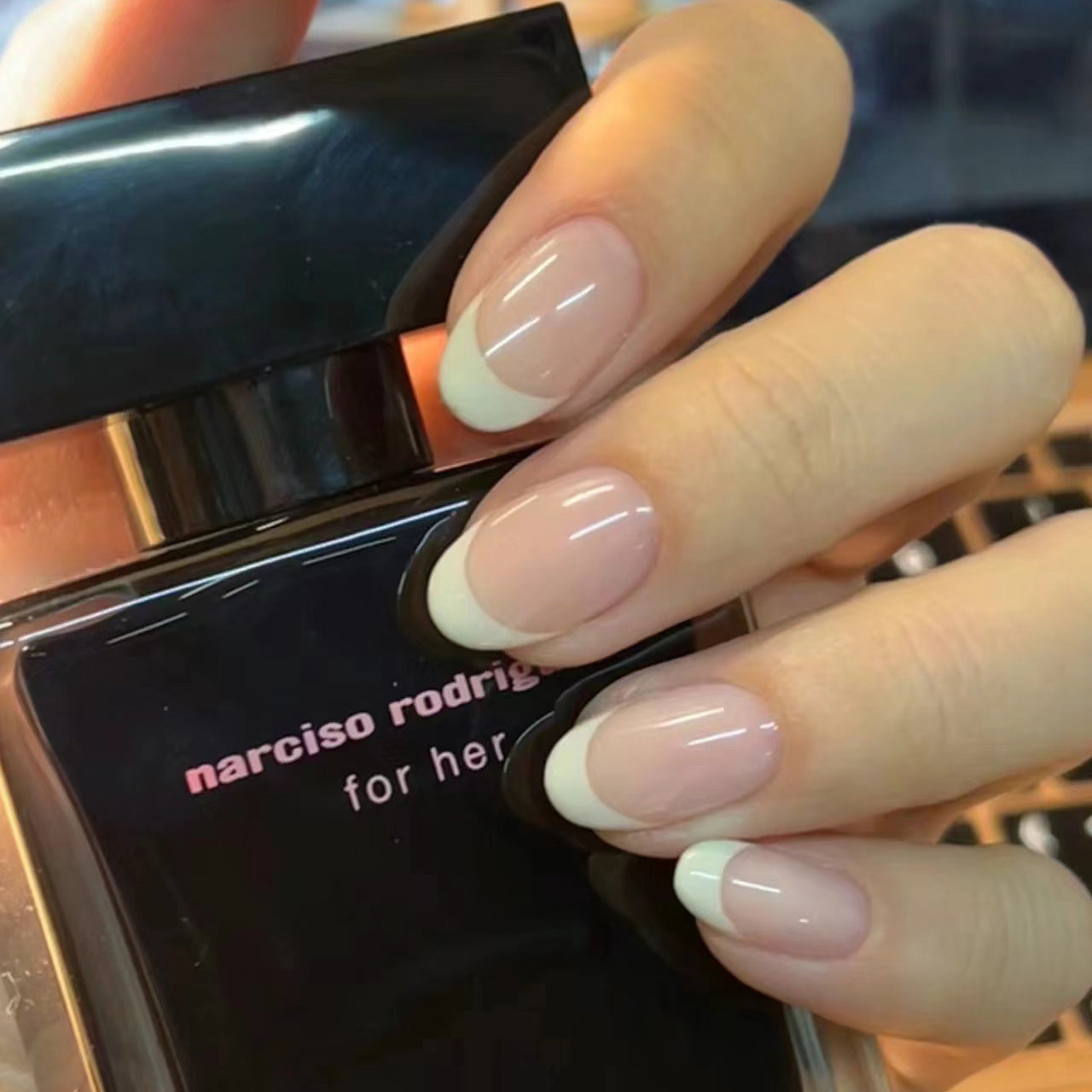 A set of beige press-on nails with a natural French tip design, displayed on a hand holding a nail polish bottle with 'Narciso Rodriguez' for her branding.