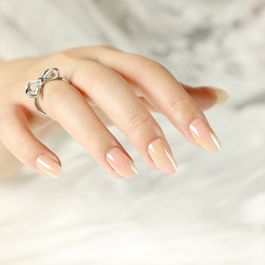 A close-up image of a person's hand with medium-sized, oval-shaped, beige-colored press-on nails featuring a subtle glow effect.