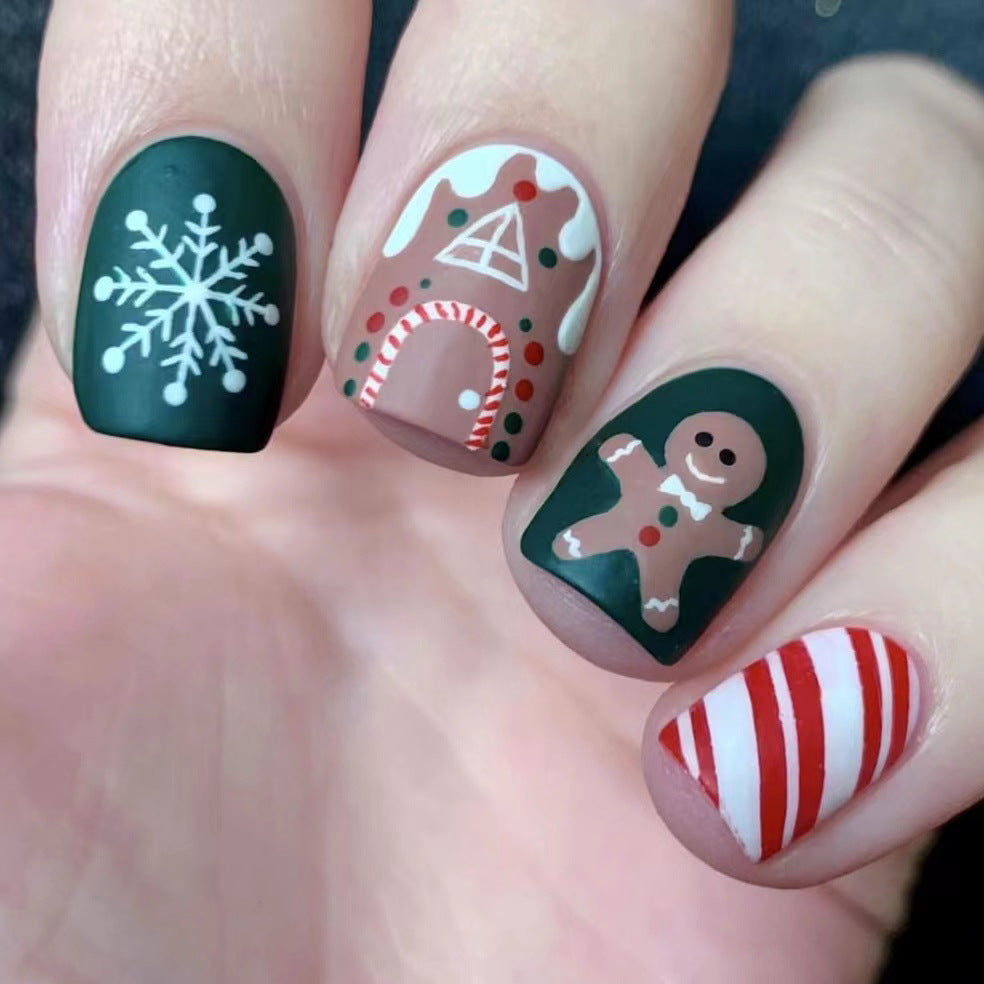 A hand showcasing press-on nails with festive green and red designs including a snowflake, a gingerbread man, and candy cane stripes.