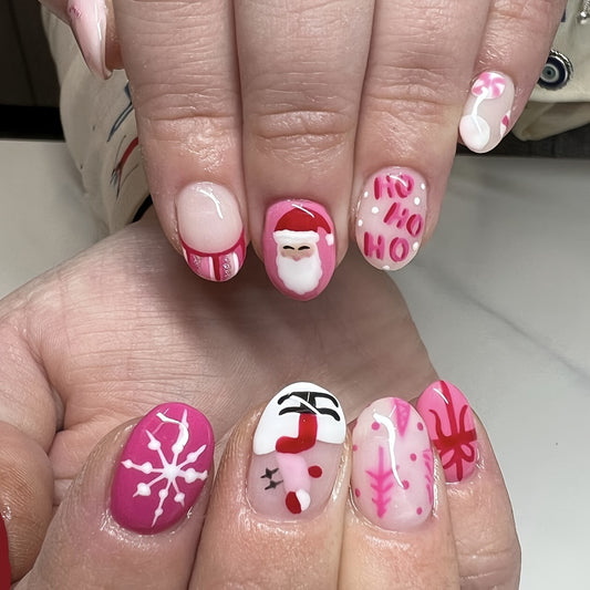 A set of pink and white press-on nails featuring Christmas-themed designs including Santa and snowflake accents.