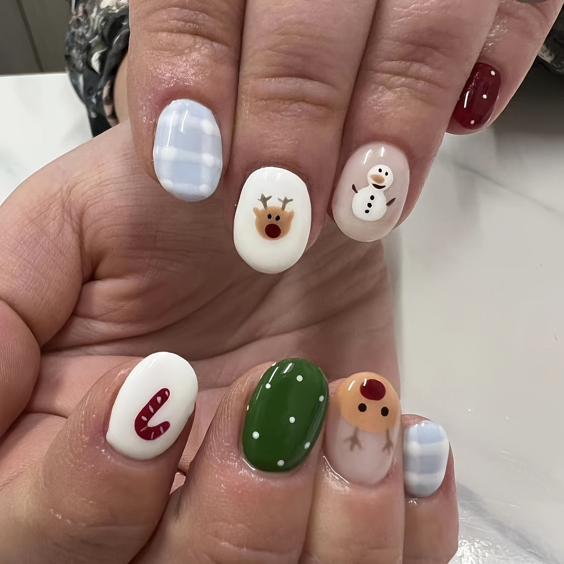 A set of short round white and green press-on nails featuring winter wonderland themed designs including a snowman and reindeer.