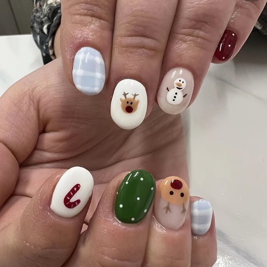 A set of short round white and green press-on nails featuring winter wonderland themed designs including a snowman and reindeer.