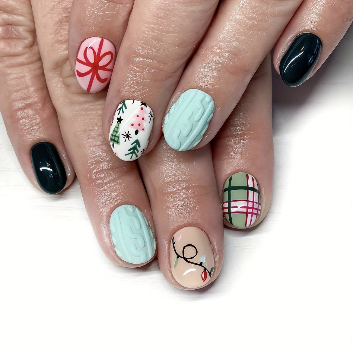 A set of short-length round press-on nails featuring pastel tones with festive holiday designs, including Christmas trees and snowflakes.