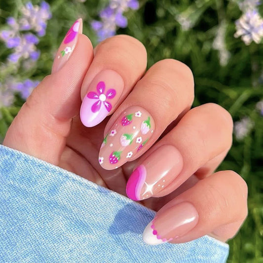 A set of press-on nails featuring floral accents and a French tip design in pastel pink color, displayed in a garden setting.