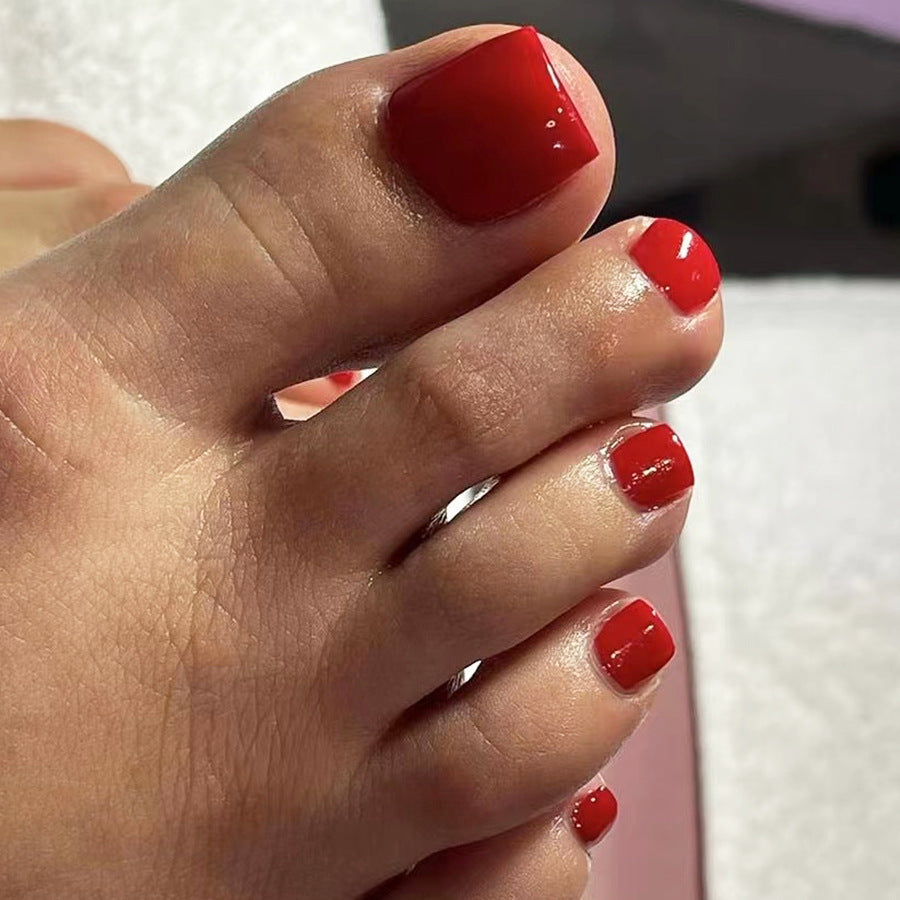 Close-up of a foot with red nail polish on toes against a neutral background