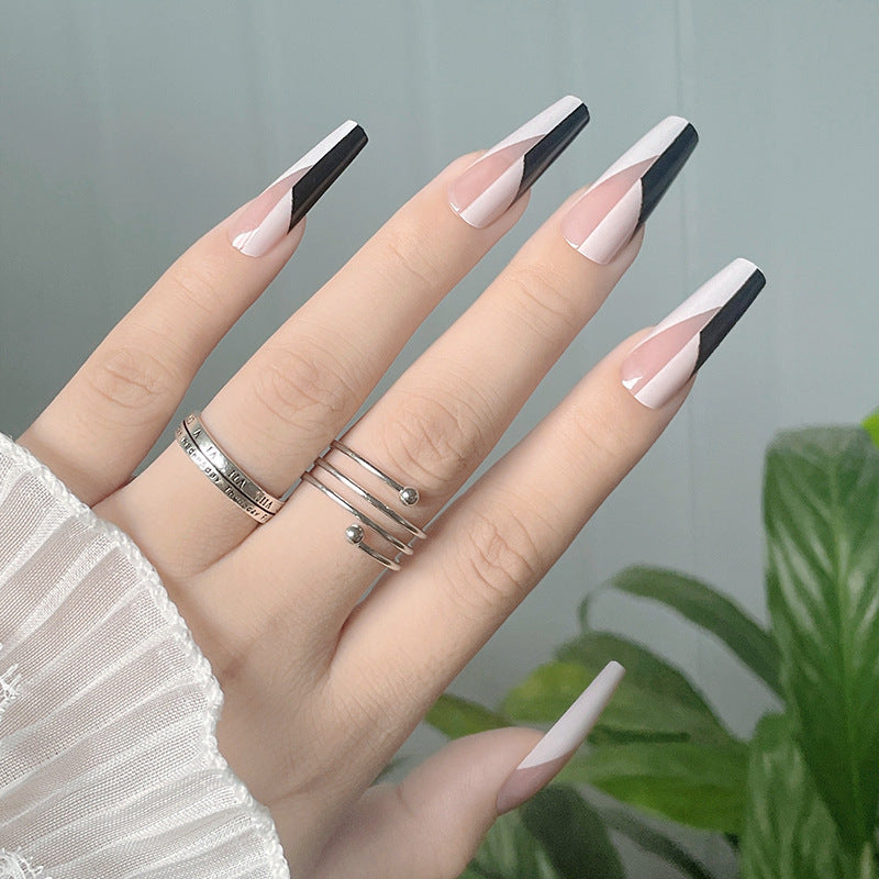 Hand with long, stylish nails featuring black and white design, wearing multiple rings on a neutral background.
