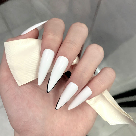 A hand with long white stiletto nails, with a press-on nail design, held under a reflective surface.