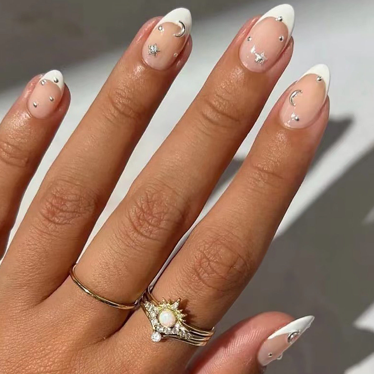 A hand with medium-sized white almond-shaped press-on nails with glitter and rhinestone detailing.