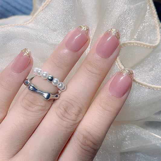 Hand with pink nails and gold accents wearing a silver ring with pearls against a light fabric background