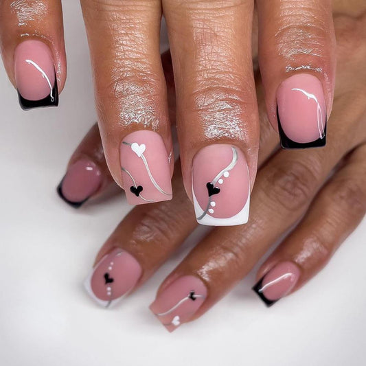 A set of pink press-on nails with a design of small white hearts and black accents on the tips.