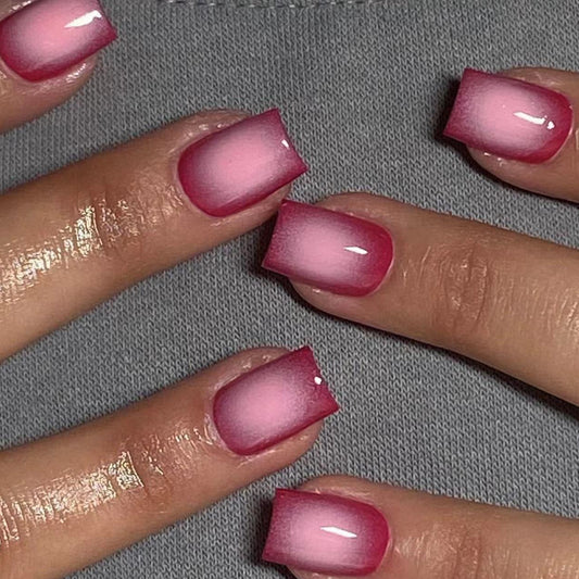A set of pink gradient press-on nails with a glossy finish, shown on a person's hands.