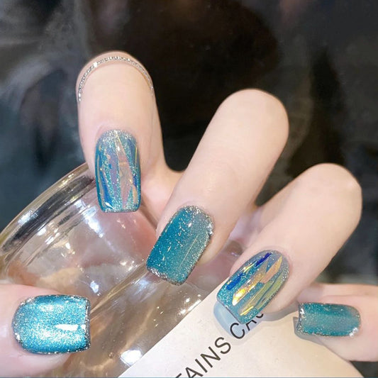 A person's hand with medium square blue glossy press on nails, holding a glass.