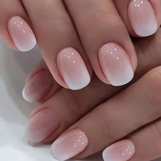 A pair of press-on nails with a natural pink to white gradient and glitter accents.