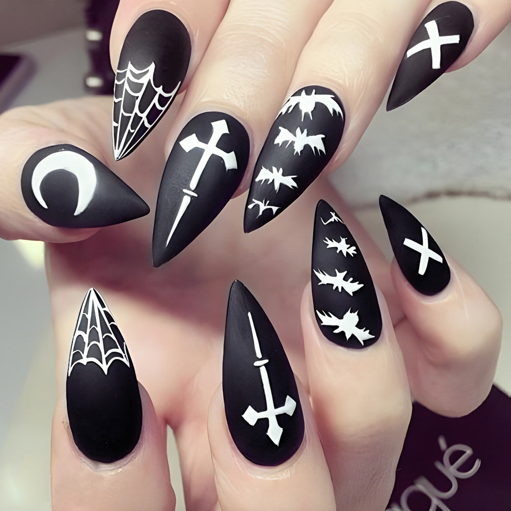 A hand showcasing press-on nails with various black designs including moons, spider webs, and crosses, indicative of a Halloween aesthetic.