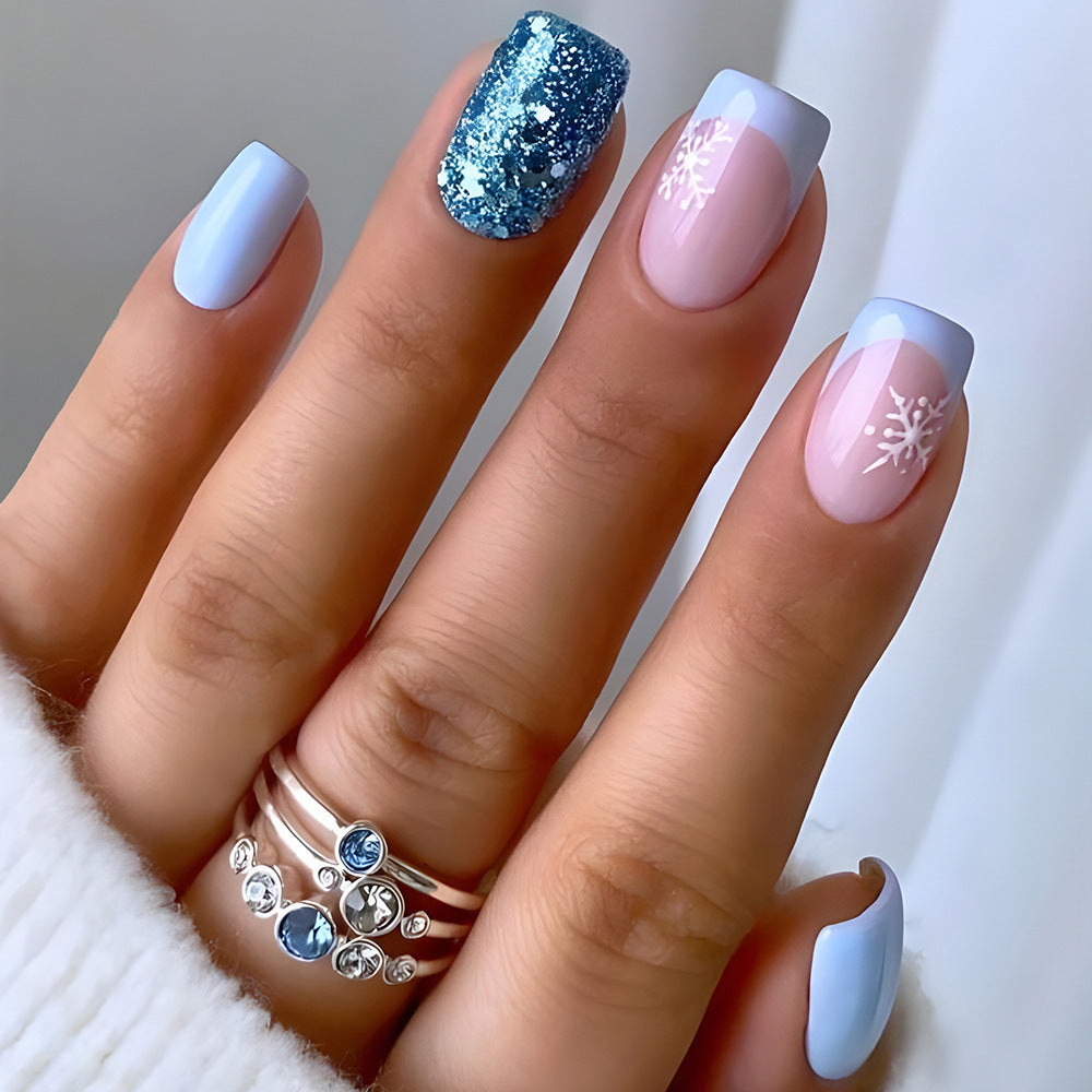 Hand with stylish nail art featuring blue glitter, pink with snowflake design, and white polish.