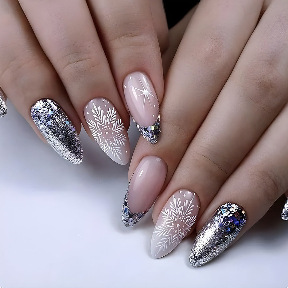 Close-up of hands with decorative nail art featuring snowflakes and glitter on a white background.