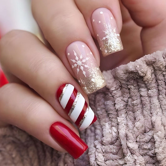 A set of long square red press-on nails with gold and white holiday design, displayed on a person's hand.