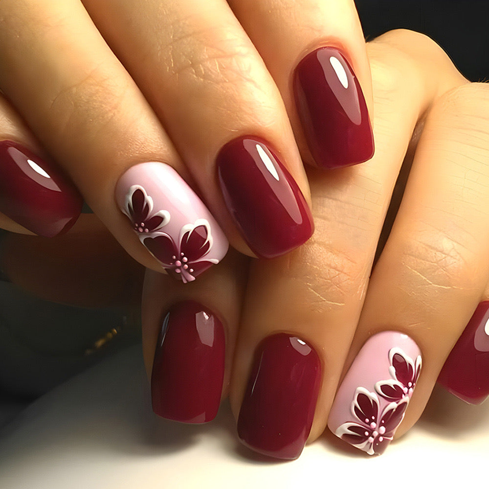 A set of short square deep burgundy press-on nails with delicate petal artwork in soft pink.