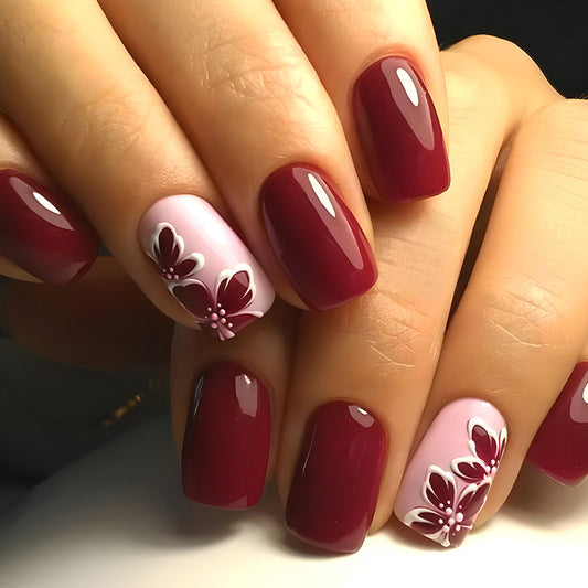 A set of short square deep burgundy press-on nails with delicate petal artwork in soft pink.