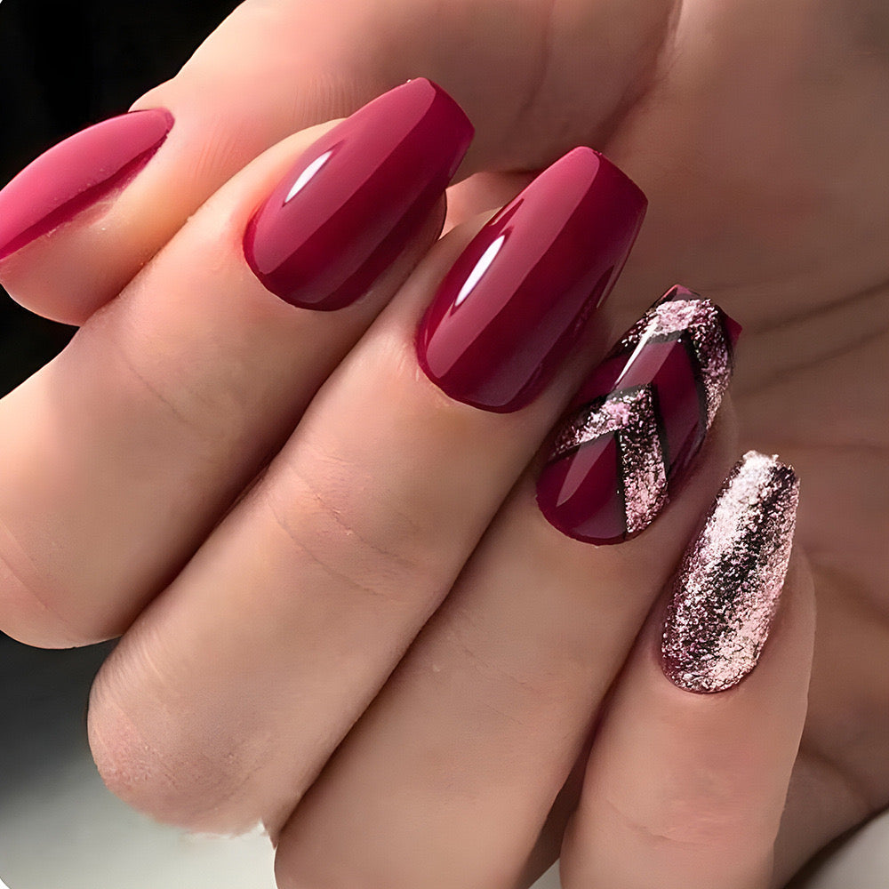 A hand with burgundy press-on nails with glitter accents, displayed in a reflective light.