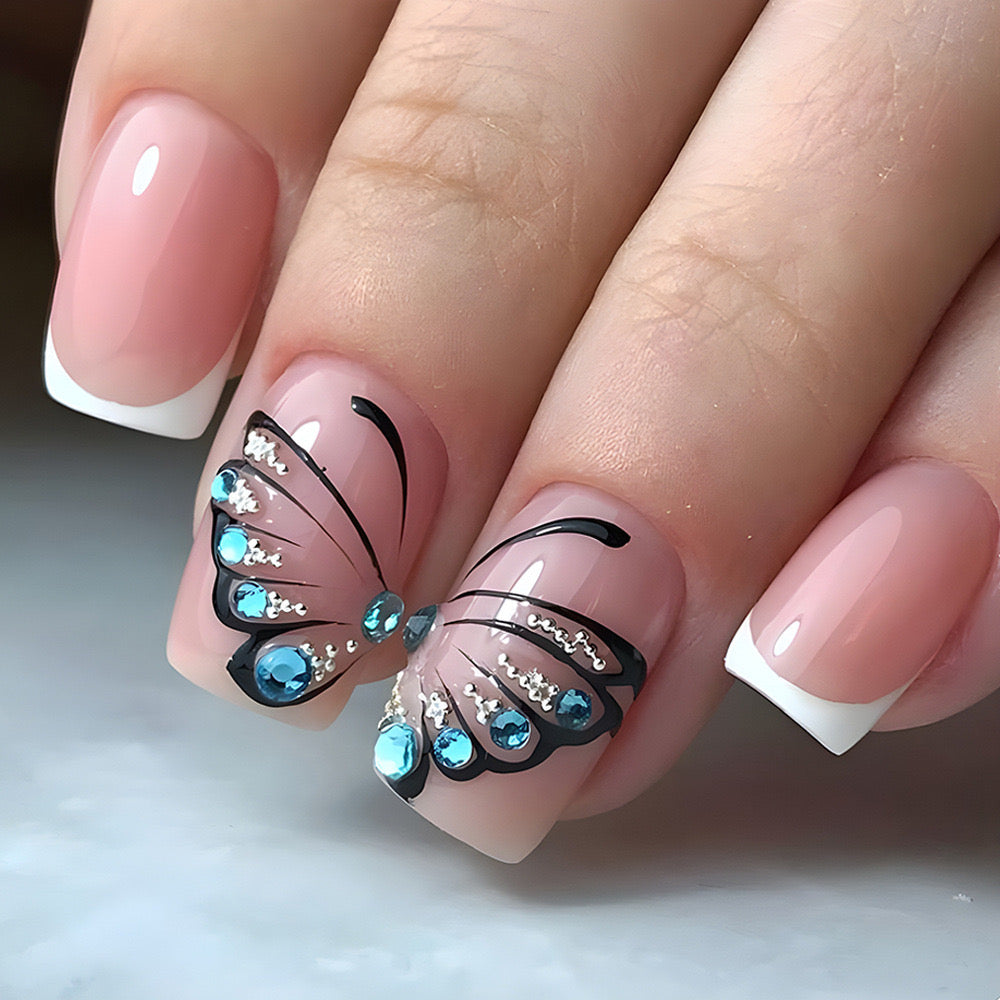 A set of blush pink press-on nails featuring a butterfly wing shape with rhinestone embellishments and a square cut.