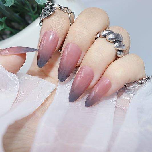 A set of extra-long almond-shaped nails with a gradient color transition from grey to blush, with a high gloss finish.