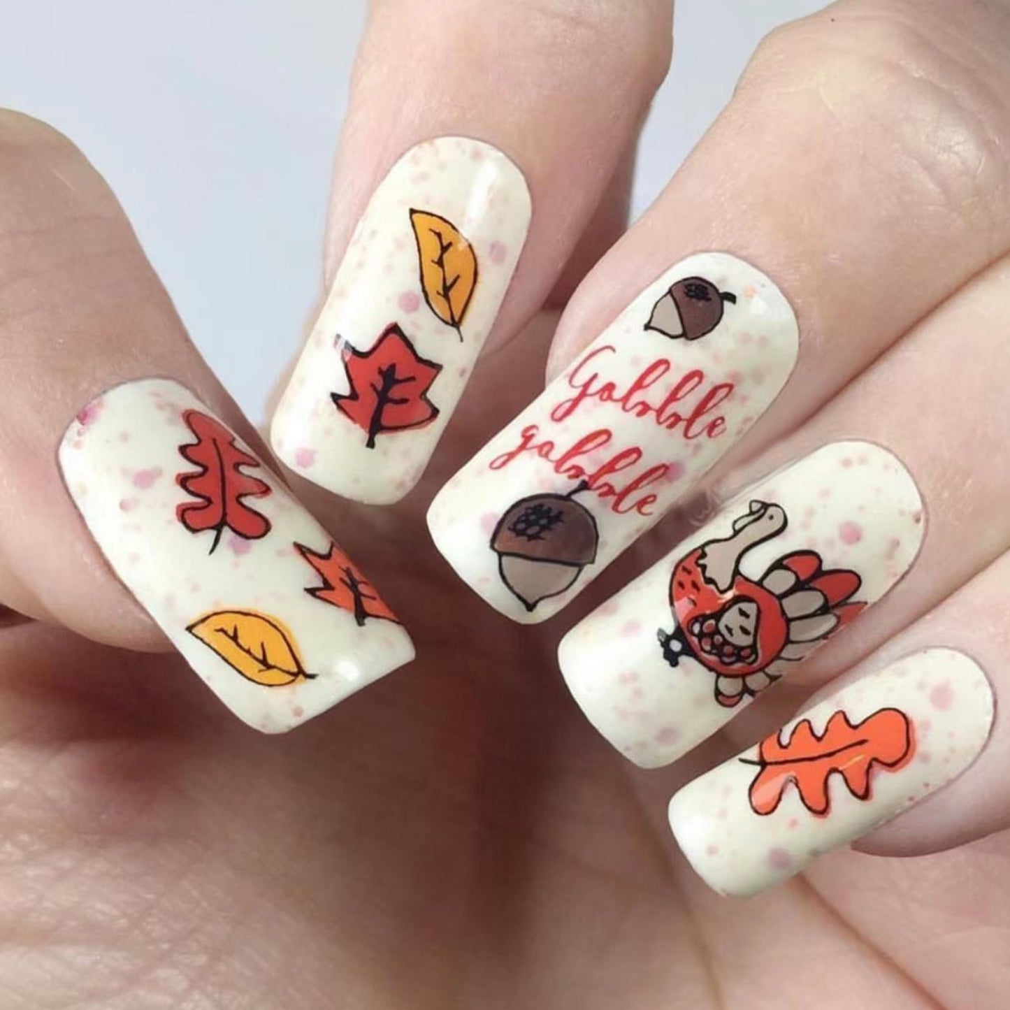 A set of press-on nails featuring a Thanksgiving-themed design with brown and beige colors and fall motifs such as leaves and a turkey.
