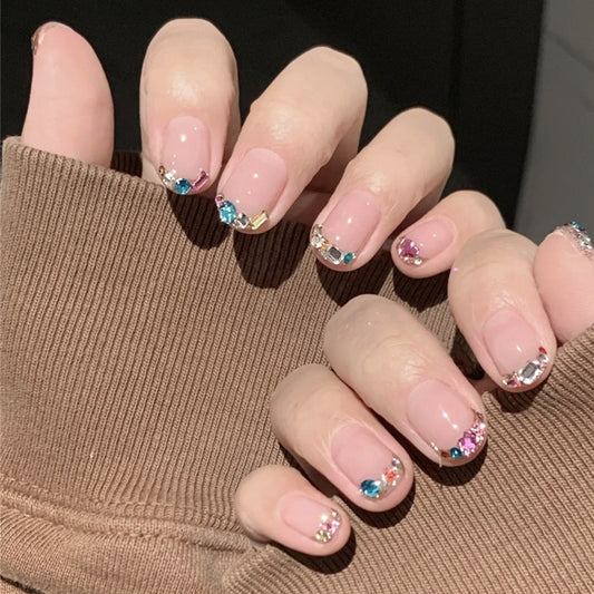 Close-up of a hand with pink nail polish and decorative gemstones, wearing a brown sleeve.