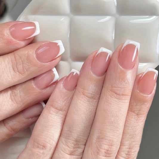 A hand with press-on nails featuring a white French tip design on a square nail shape.