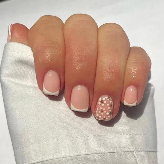 A hand with short square white French tips press on nails, with one nail having a polka dot design.