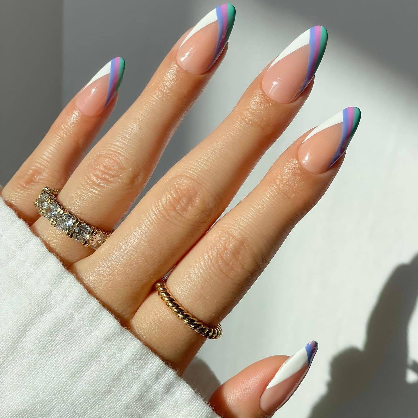 A set of beige almond-shaped press-on nails with multicolor accents, displayed on a person's hands.