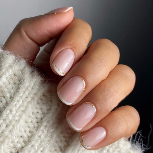 A close-up of a person's hand showing short squoval-shaped press-on nails with a white French tip design. The nails are attached to a knitted sweater, suggesting a stylish and casual look.