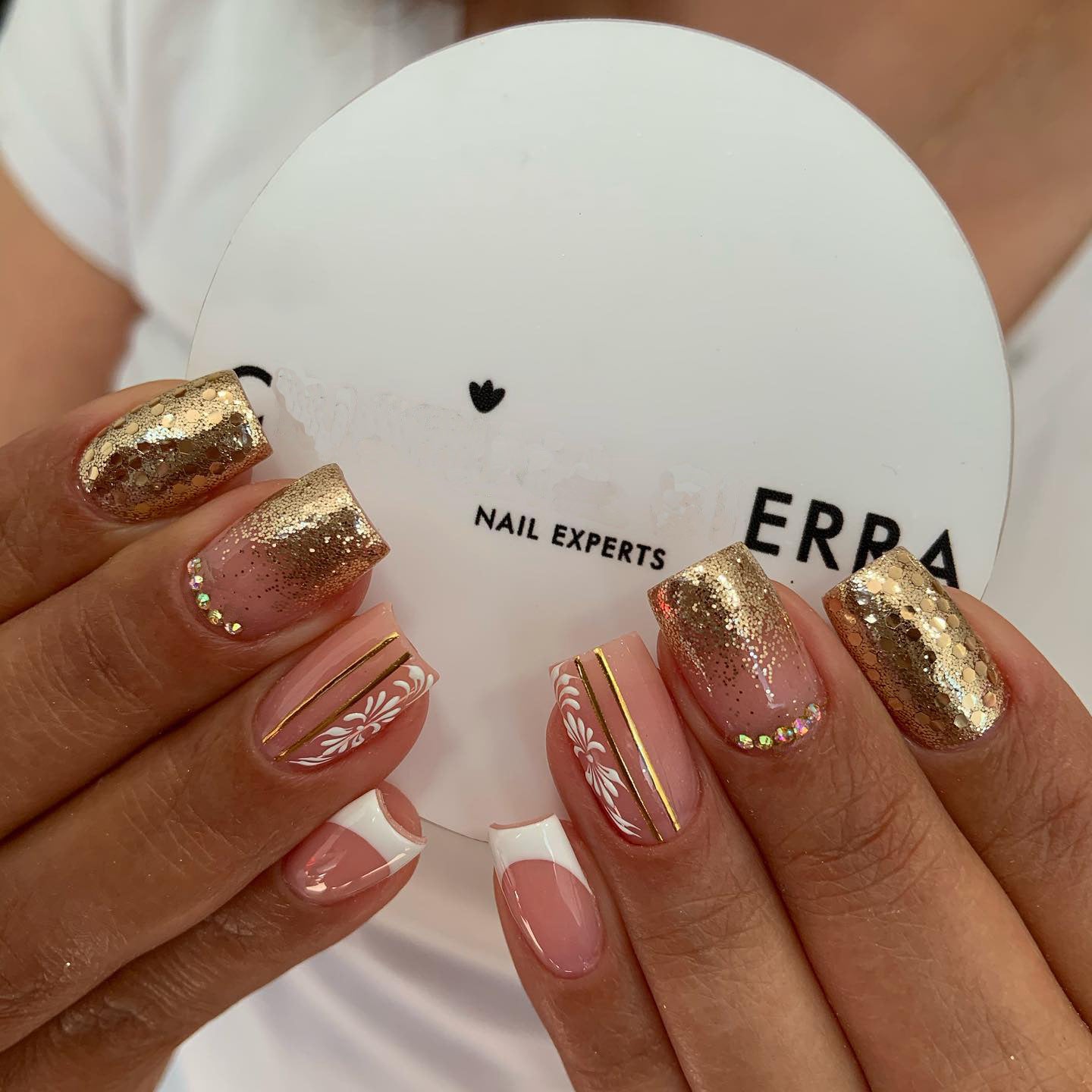 Close-up of hands with decorative nails holding a white compact mirror with 'ERBA' branding.