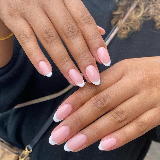 A pair of hands showcasing press-on nails with a white French tip design on an oval-shaped nail.