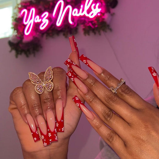 A pair of long, red floral press-on nails displayed in a glossy finish with pink detailing around the edges.