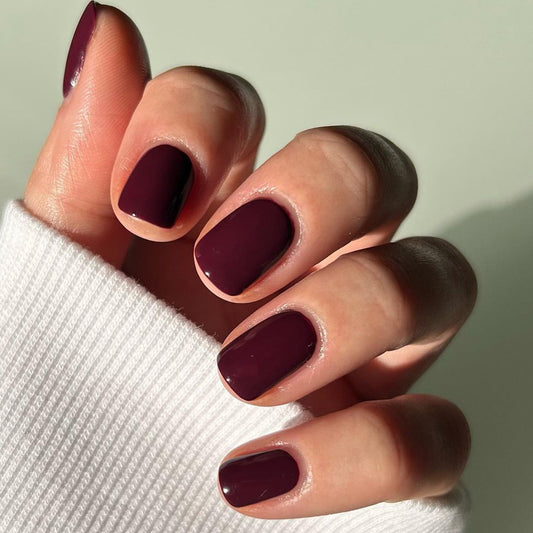 A hand with short squoval shaped red press-on nails, wearing a white sweater.