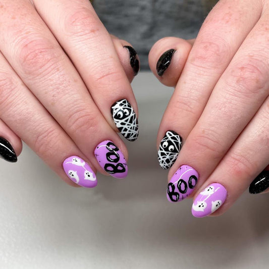 A person's hands displaying press-on nails with a Halloween theme, featuring purple nails with 'BOO' text and black and white patterned nails.