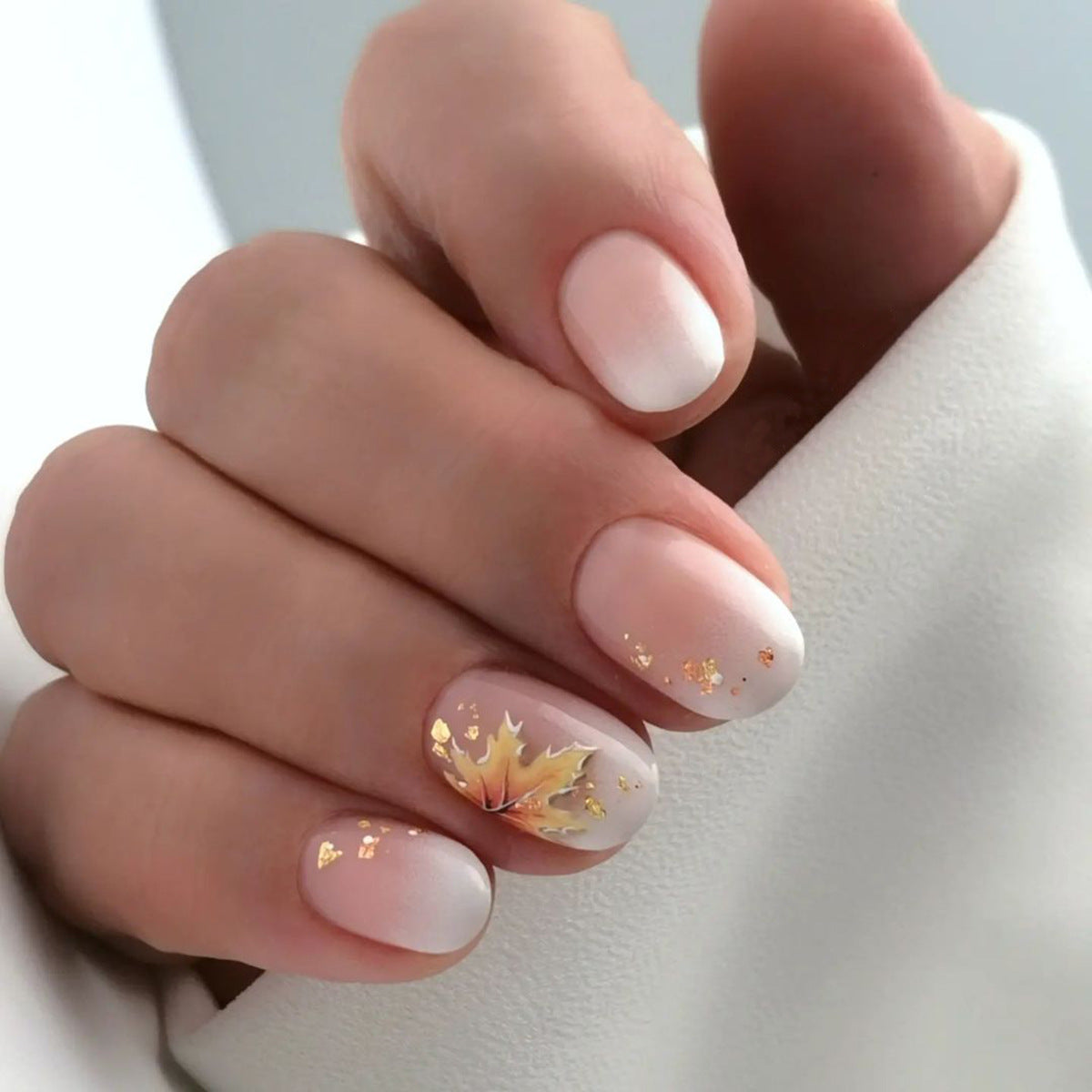 A set of short round gold-colored press-on nails with a fall theme, showcasing a gold leaf pattern.