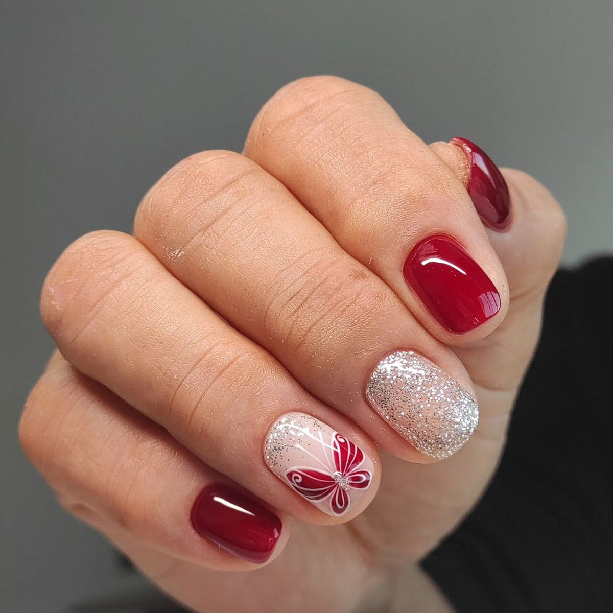 Hand with red and silver nail polish on a gray background