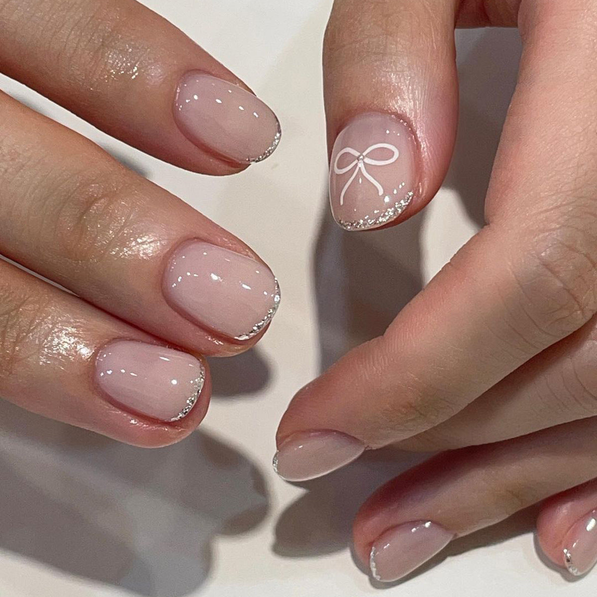A photo showing a set of press-on nails in a beige color with a decorative element on the ring finger.