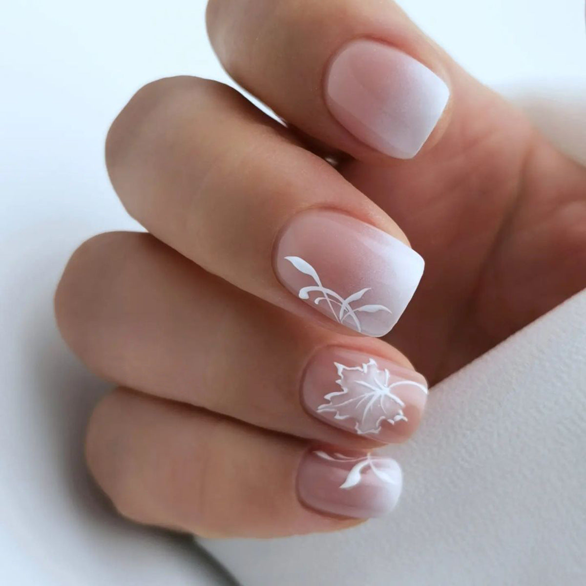 Close-up of a hand with white floral nail art on a light background