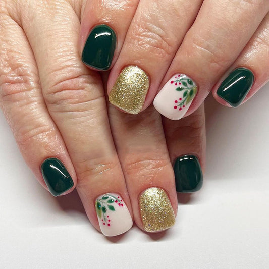 A set of short square green press-on nails with gold accents and red holly designs.