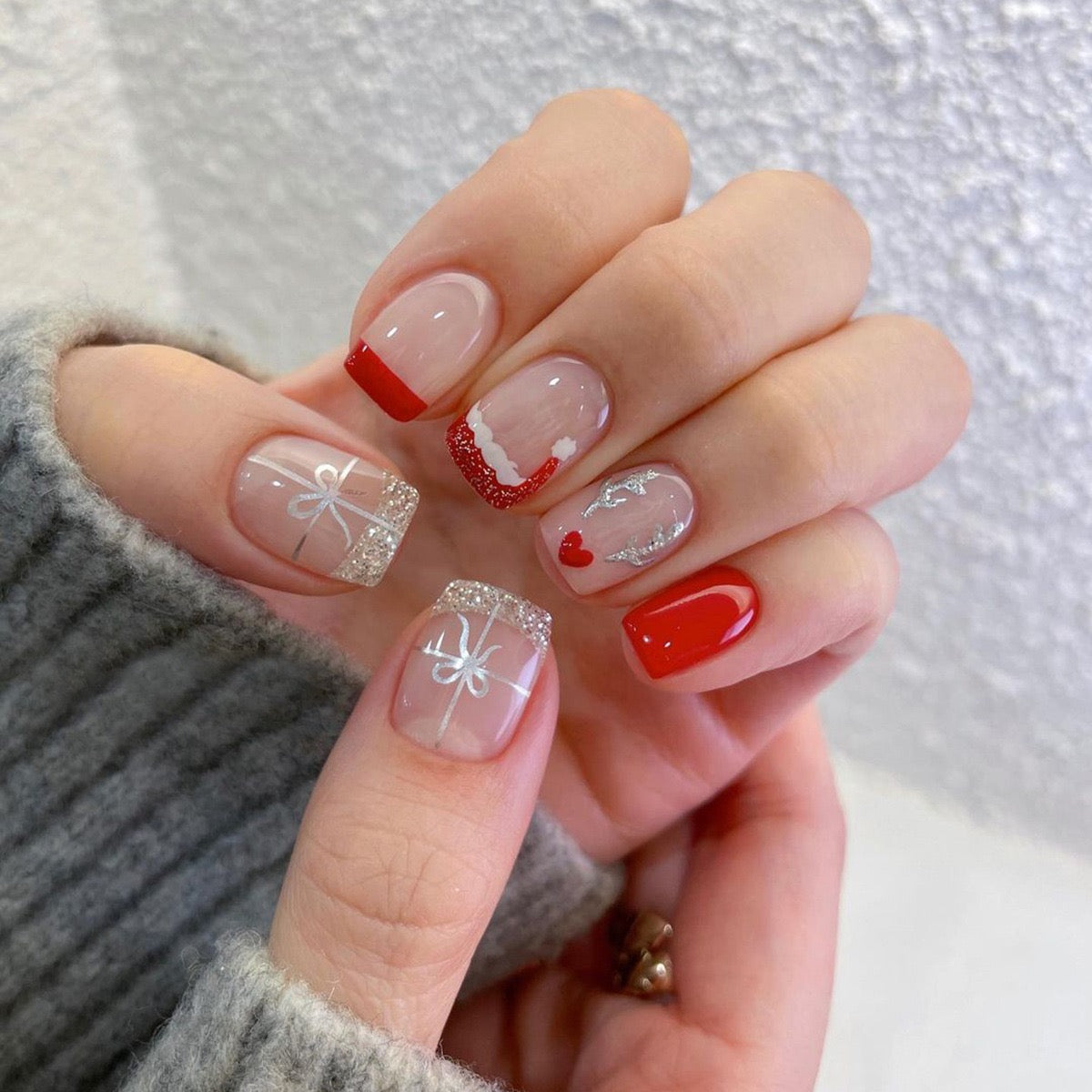 Hand with red and clear nail art on a textured white background