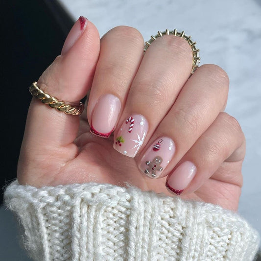 A person's hand with press-on nails featuring a beige base with red and white Christmas-themed decorations, such as snowflakes and stars.
