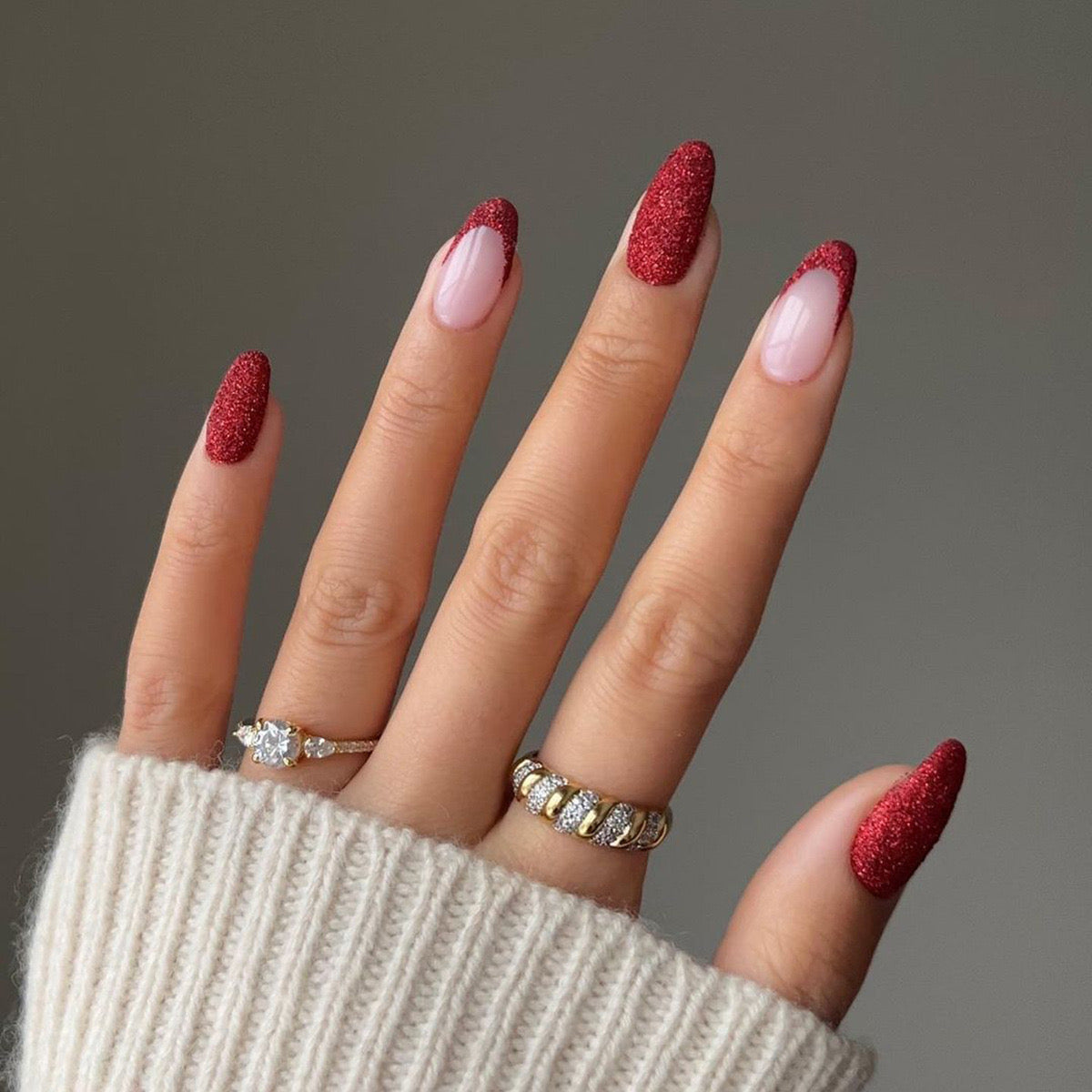 A person's hand with press-on nails featuring a medium almond shape with a color gradient from burgundy at the tips to blush glitter at the cuticles.